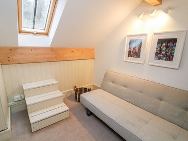 A small room with a beige sofa a wicker basket wooden steps and framed pictures on the wall at Sunshine Cottage in Preston under Scar near Leyburn