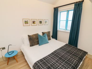 A bedroom with a double bed with pillows a bedside table with a lamp a window with curtains and framed pictures on the wall at Sunshine Cottage in Preston under Scar near Leyburn