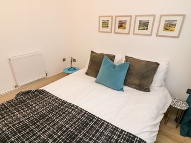A bedroom with a bed with pillows and a blanket and framed pictures on the wall at Sunshine Cottage in Preston under Scar near Leyburn