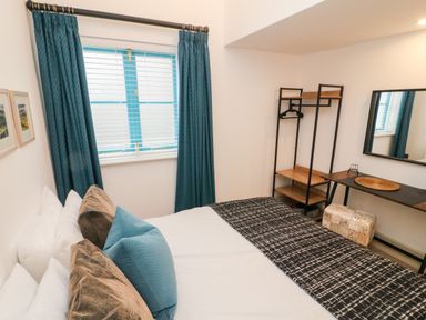 A bedroom with a bed pillows window with curtains clothes rack desk and mirror at Sunshine Cottage in Preston under Scar near Leyburn