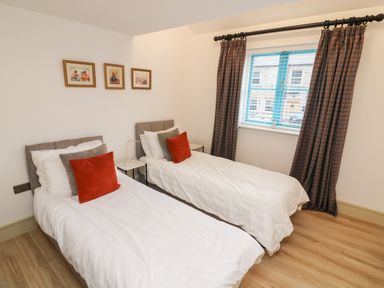 A bedroom with two single beds with white bedding and red pillows a window with curtains and three paintings on the wall at Sunshine Cottage Preston under Scar near Leyburn