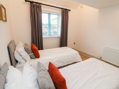 A bedroom with two single beds white bedding cushions and a window with curtains at Sunshine Cottage in Preston under Scar near Leyburn