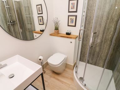 A bathroom with a shower enclosure a toilet a sink and a round mirror at Sunshine Cottage in Preston under Scar near Leyburn