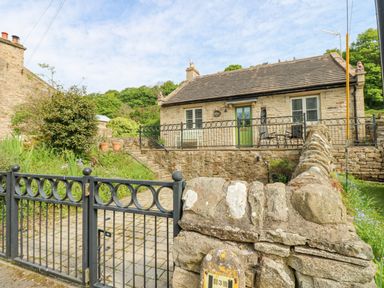 Stone cottage with green door and windows behind black metal gate and stone wall at Sunshine Cottage in Preston under Scar near Leyburn