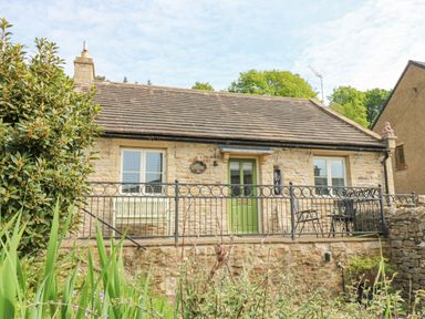 A stone cottage with a green door two windows and metal railing in front at Sunshine Cottage in Preston under Scar near Leyburn