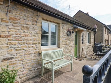 A stone cottage exterior with a green door bench and outdoor table and chairs at Sunshine Cottage in Preston under Scar near Leyburn
