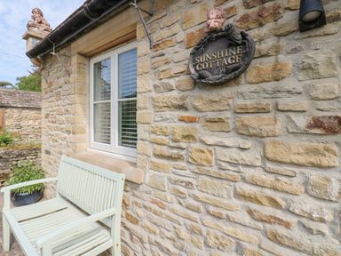 A stone cottage exterior with a white bench and a Sunshine Cottage sign at Sunshine Cottage in Preston under Scar near Leyburn