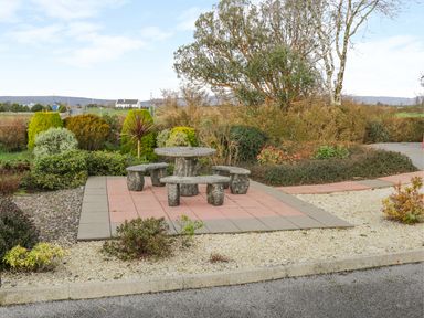 A stone table with four stone benches on a tiled area surrounded by plants and bushes at Ellens Cottage in Mount Charles County Donegal