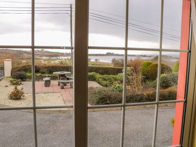 A view through window showing a garden with stone table and benches bushes and a lake in the background at Ellens Cottage Mount Charles County Donegal