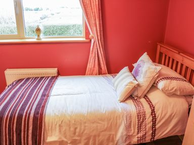 A bedroom with a single bed and striped bedding next to a window with curtains at Ellens Cottage in Mount Charles County Donegal