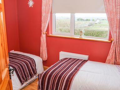 A bedroom with two single beds with striped blankets near a window with pink curtains at Ellens Cottage in Mount Charles County Donegal