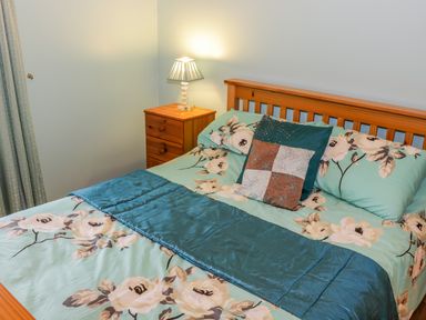A bedroom with a wooden bed frame a floral bedspread and a nightstand with a lamp at Ellens Cottage Mount Charles County Donegal