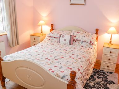 A bedroom with a double bed floral bedding two bedside tables with lamps and a window at Ellens Cottage in Mount Charles County Donegal