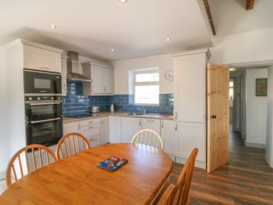 A kitchen with white cabinets blue backsplash wooden dining table and chairs at Macreddin Rock Holiday Cottage Macreddin Aughrim County Wicklow