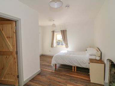A bedroom with a single bed beside a dresser and a window with curtains at Macreddin Rock Holiday Cottage Macreddin Aughrim County Wicklow