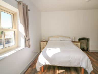 A bedroom with a double bed flanked by two nightstands and a small arched fireplace with a plant at Macreddin Rock Holiday Cottage Macreddin Aughrim County Wicklow