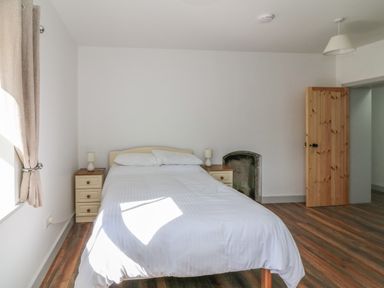 A bedroom with a double bed with white bedding two bedside tables with lamps wooden door and window with curtains at Macreddin Rock Holiday Cottage Macreddin Aughrim County Wicklow