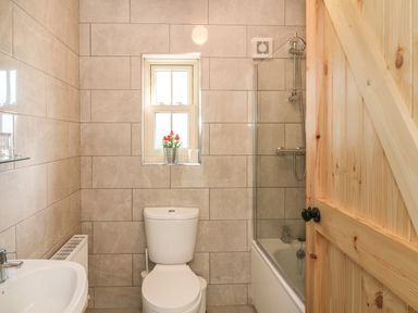 A bathroom with a toilet sink shower window and a wooden door at Macreddin Rock Holiday Cottage Macreddin Aughrim County Wicklow