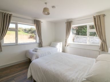 A bedroom with two beds and beige curtains on windows at Macreddin Rock Holiday Cottage in Macreddin Aughrim County Wicklow