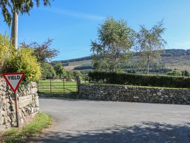 A rural road intersection with stone walls yield sign and metal gate with hills and trees in the background at Macreddin Rock Holiday Cottage Macreddin Aughrim County Wicklow