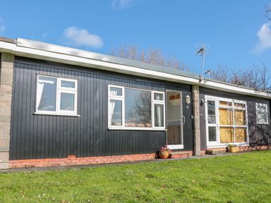 A single story building with black wooden siding windows and a door on a grassy area at The Borrowers in Dartmouth