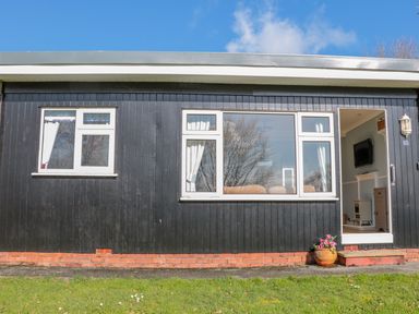 The exterior of a black wooden building with white framed windows and an open door showing a television and stove inside at The Borrowers in Dartmouth