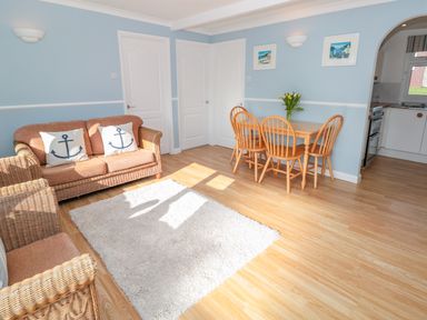 A living room with wicker sofa and armchair pillows with anchors wooden dining table and chairs with flowers on table at The Borrowers in Dartmouth