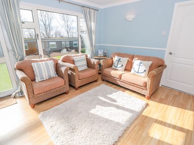 A seating area with wicker armchairs and a loveseat with cushions by large windows in a room at The Borrowers in Dartmouth