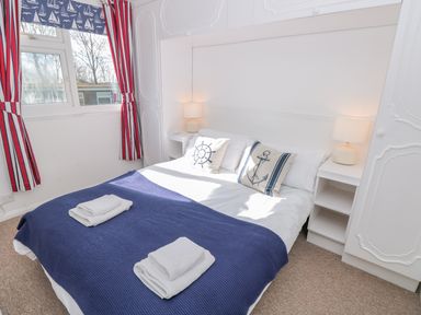 A bedroom with a double bed blue blanket and nautical themed pillows near a window with striped curtains at The Borrowers in Dartmouth