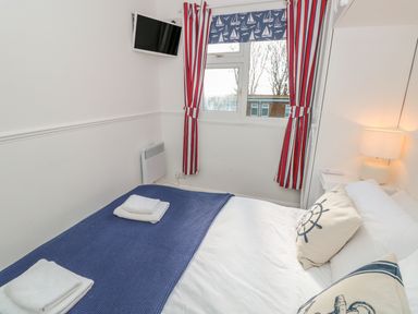 A bedroom with a bed with folded towels bedside lamps a window with striped curtains and a wall-mounted tv at The Borrowers in Dartmouth