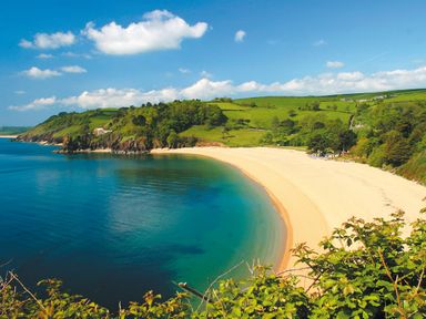 A beach with clear water and green hills in the background at The Borrowers in Dartmouth