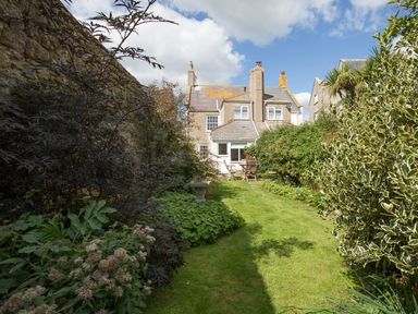 A garden with grass, bushes, a birdbath, and a table with chairs by a house at Brock Cottage in West Bay