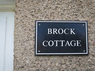 A black and white sign reading Brock Cottage mounted on a pebble textured exterior wall