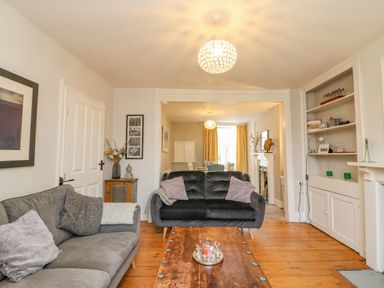 A living room with two sofas, a wooden coffee table, shelves with decorations, and a view into a dining area at Brock Cottage in West Bay