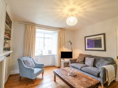 A living room with a gray sofa and blue armchair wooden floor and a coffee table at Brock Cottage in West Bay
