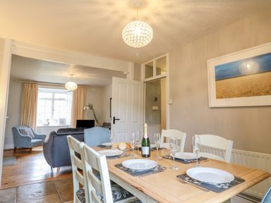 A dining area with a wooden table set with plates and glasses adjacent to a living room with blue and gray chairs at Brock Cottage in West Bay