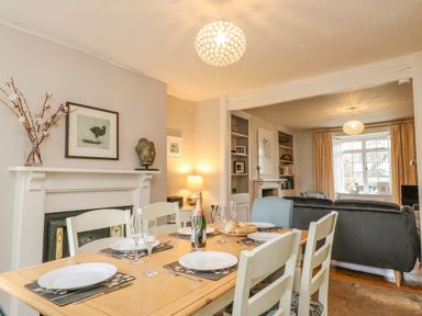 A dining table set for four with plates and glasses next to a fireplace in a room connecting to a living area with sofas at Brock Cottage West Bay