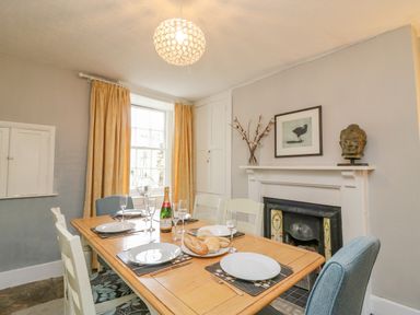 A dining room with a set table a fireplace a window with curtains and wall art at Brock Cottage in West Bay