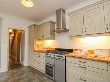A kitchen with beige cabinets a stainless steel stove and oven wooden countertops and a door leading to a hallway at Brock Cottage in West Bay