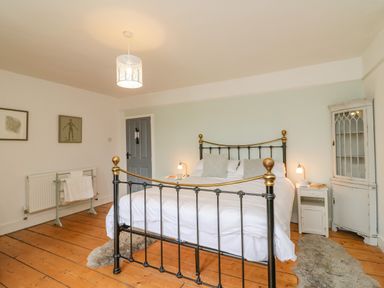 A bedroom with a black metal bed frame wooden floor bedside tables and a cabinet at Brock Cottage in West Bay