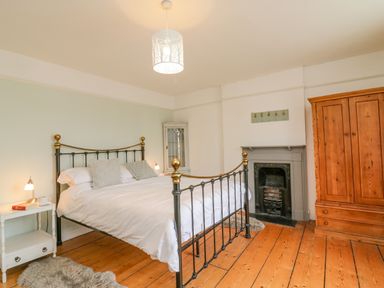 A bedroom with a metal bed frame wooden wardrobe fireplace and bedside tables at Brock Cottage in West Bay