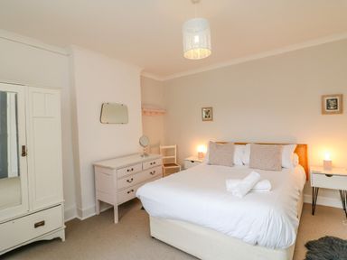 A bedroom with a bed with pillows and towels bedside tables with lamps a dresser a chair and a wardrobe at Brock Cottage in West Bay