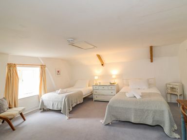 A bedroom with two single beds a central chest of drawers two lamps a window with curtains and a chair at Brock Cottage in West Bay