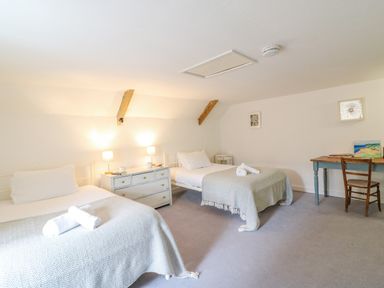 A bedroom with two single beds a chest of drawers with lamps and a desk with a chair at Brock Cottage in West Bay