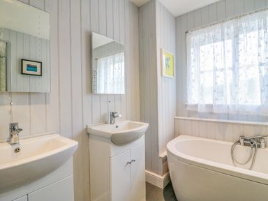 A bathroom with two sinks under mirrors and a bathtub next to a window with sheer curtains at Brock Cottage in West Bay