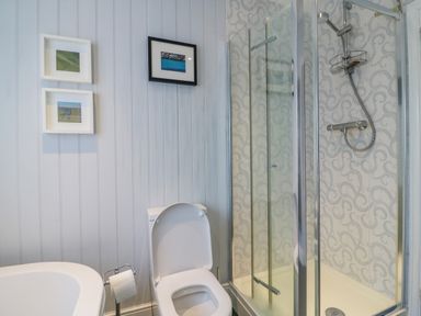 A bathroom with a toilet a shower with glass doors and wall art at Brock Cottage in West Bay