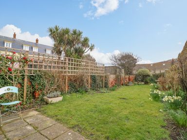 A garden with green grass flowers and a metal chair near a paved area at Brock Cottage in West Bay