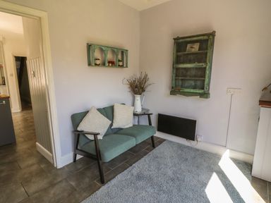A small sitting area with a two-seater sofa with cushions a side table with a pitcher of dried flowers on it and antique wall shelves at Brock Cottage in West Bay