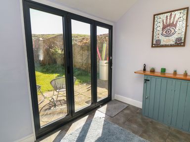 A room with sliding glass doors leading to an outdoor patio with two chairs and a garden at Brock Cottage in West Bay