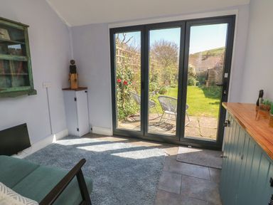 A room with glass doors opening to a garden with two chairs and a paved patio at Brock Cottage in West Bay